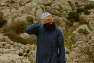 Man in een navy qamis met witte kufi in het rotslandschap van El Torcal