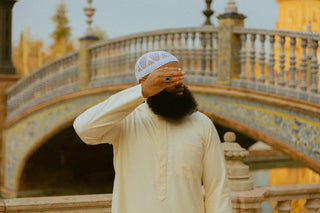 Man in een crèmekleurige qamis met witte kufi bij een brug op de Plaza de España in Sevilla