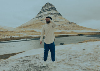 Man in een lang shirt en een ruime broek met boord bij de enkel, voor de berg Kirkjufell in IJsland
